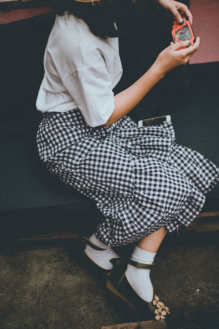 Girl in checkered skirt playing a handheld game outdoors in Hanoi, Vietnam.